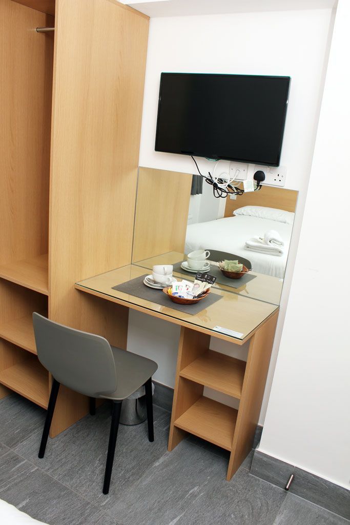 A hotel room with a desk , chair , television and mirror.
