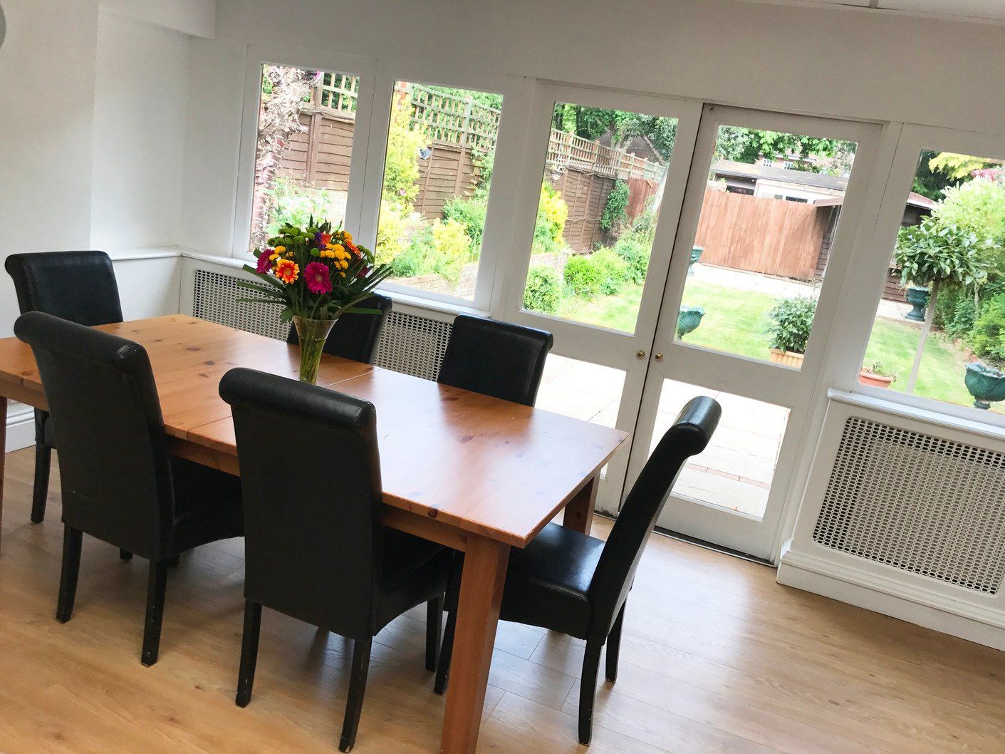 A dining room with a table and chairs and a vase of flowers.