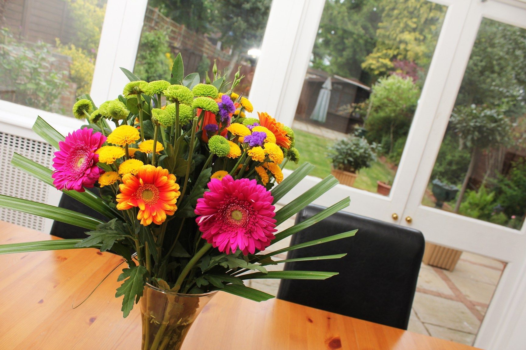 A vase filled with colorful flowers sits on a wooden table.