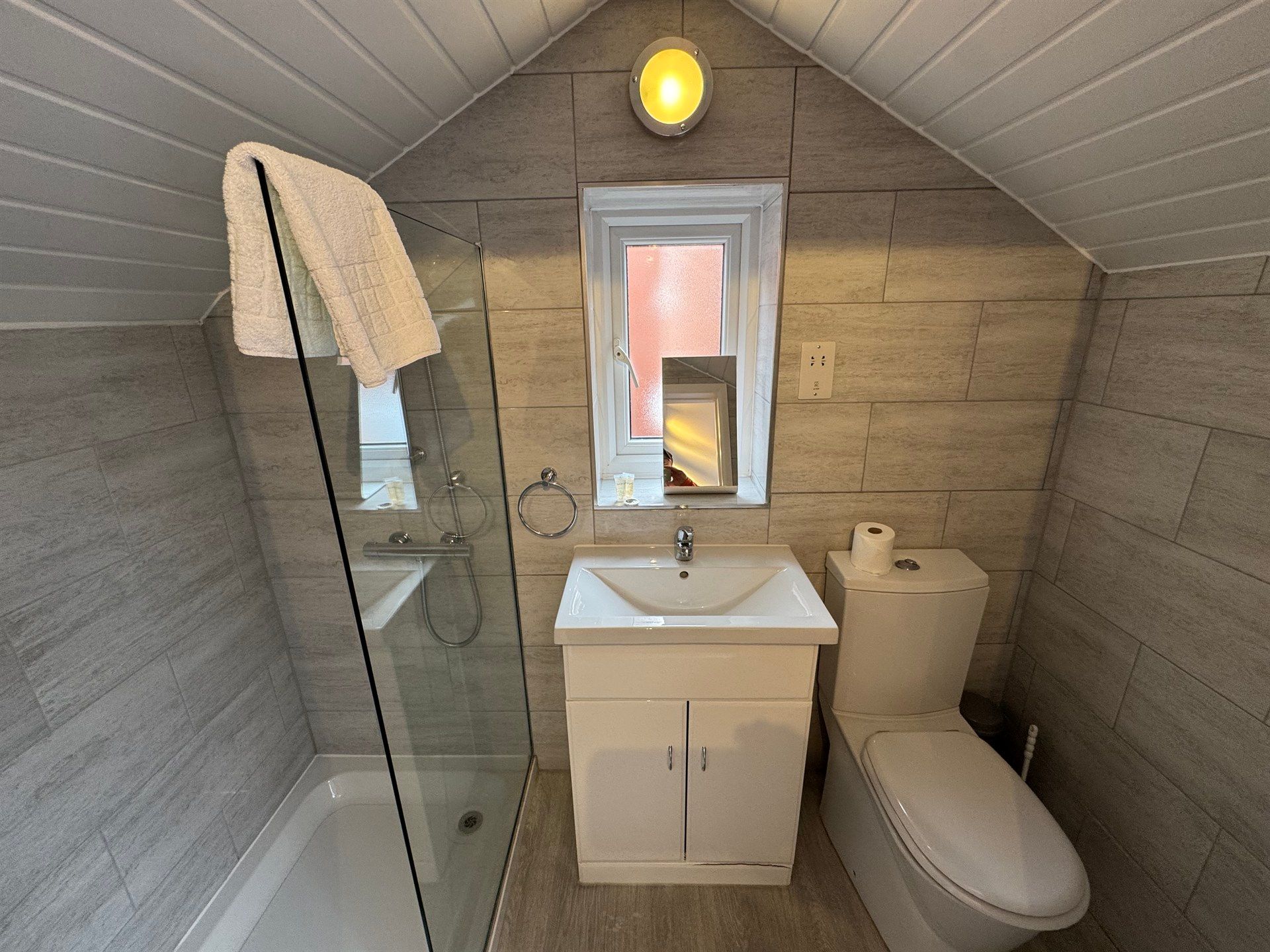 A bathroom with a sink , toilet , shower and window.