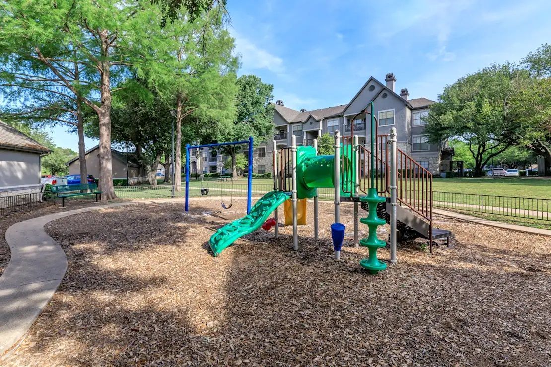 A playground with a slide, swings, and stairs in front of a building.