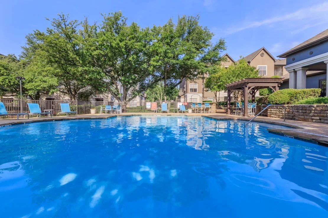 A large swimming pool surrounded by trees and chairs in a residential area.