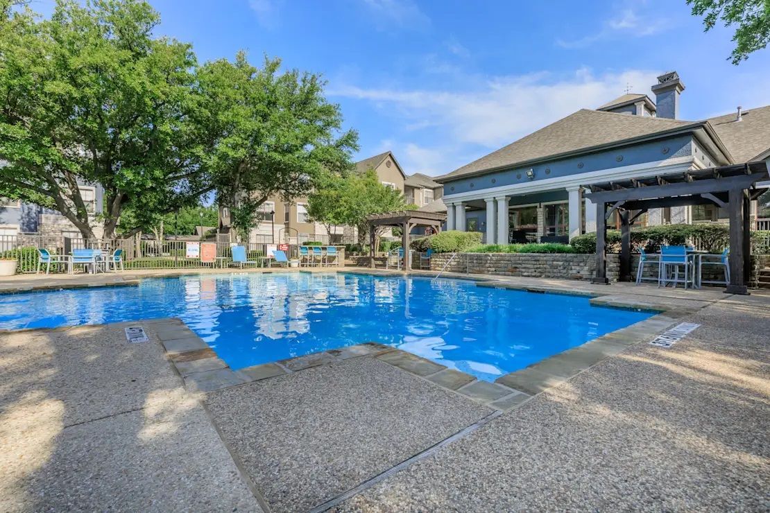 A large swimming pool in front of a house with a pergola.