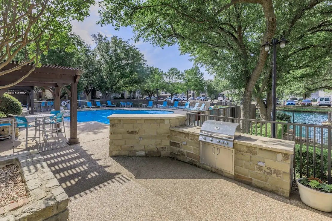 A patio with a grill and a pool in the background.