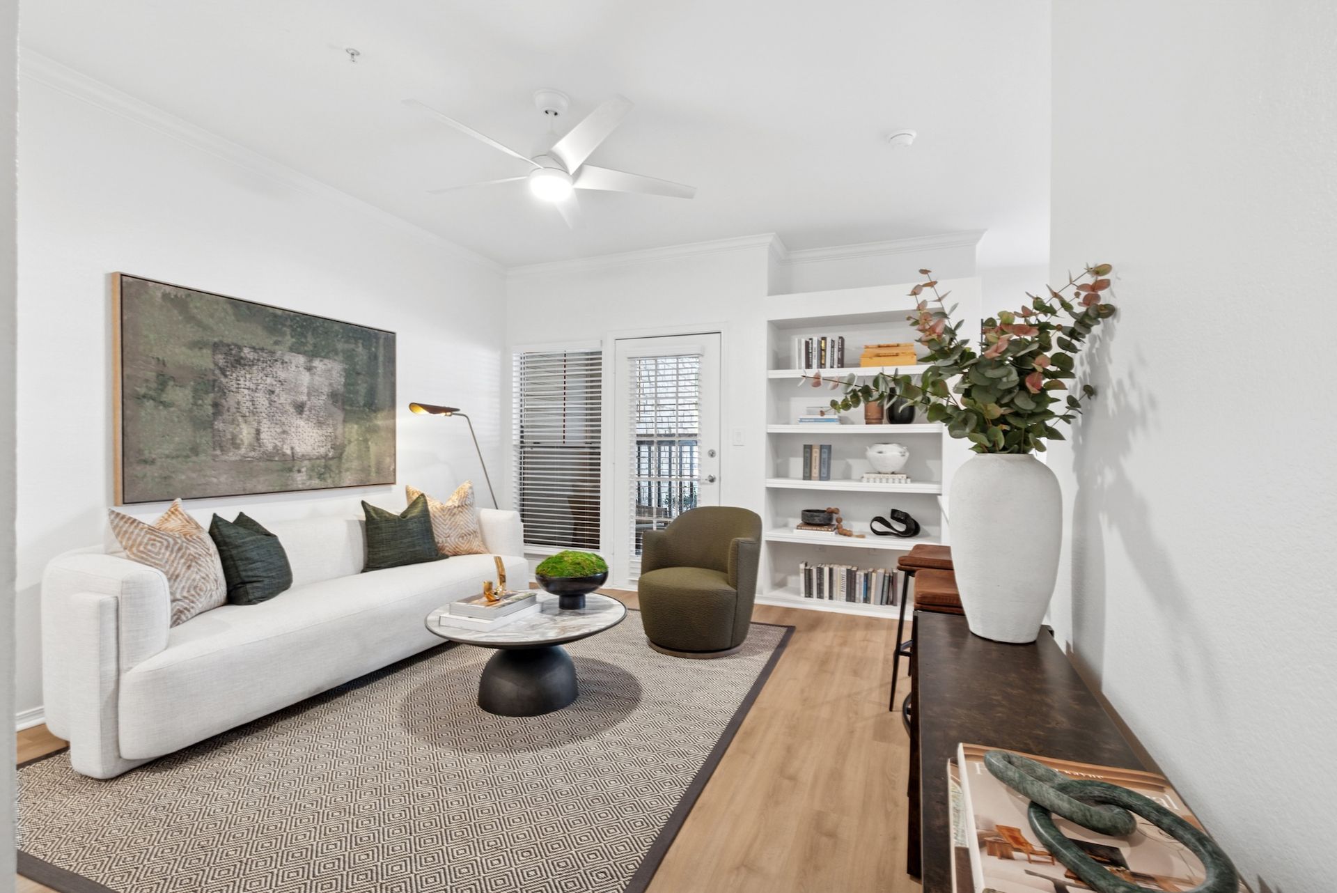 Living room with white sofa, green chair, rug, built-in shelves, and artwork.