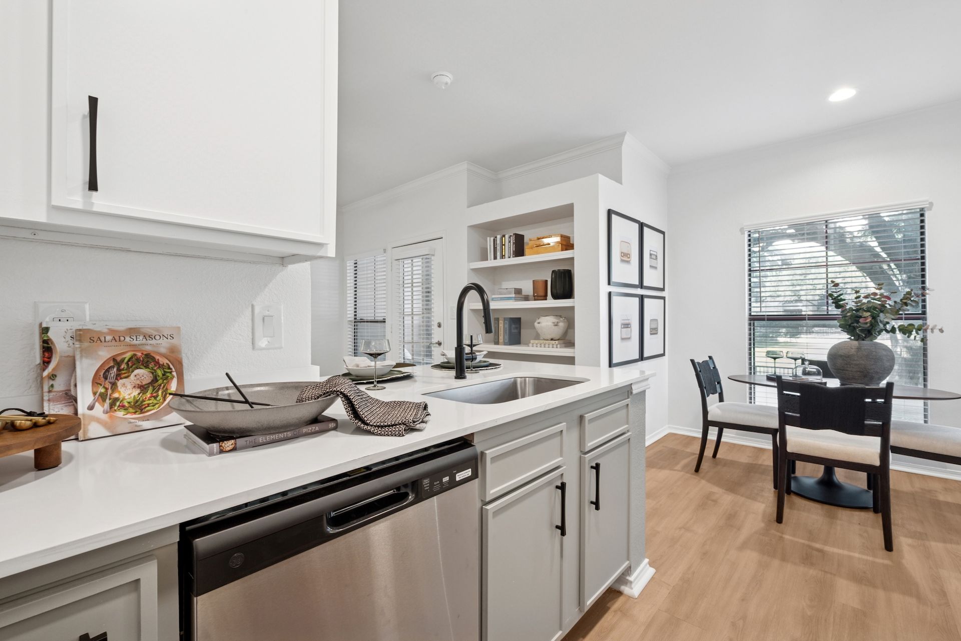 Kitchen with white cabinets, gray counters, and stainless steel appliances; a dining area in the background.