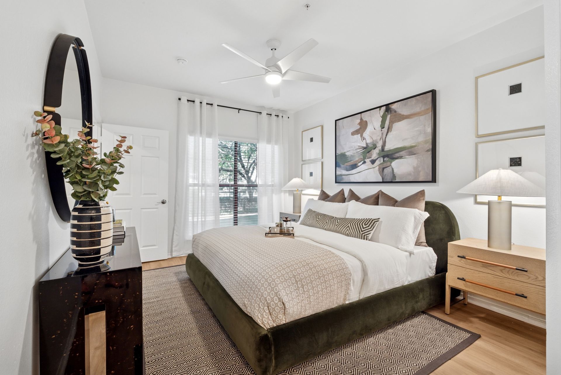 Bedroom with green bed, neutral rug, and white walls. Dark dresser with mirror. Sunlight through window.