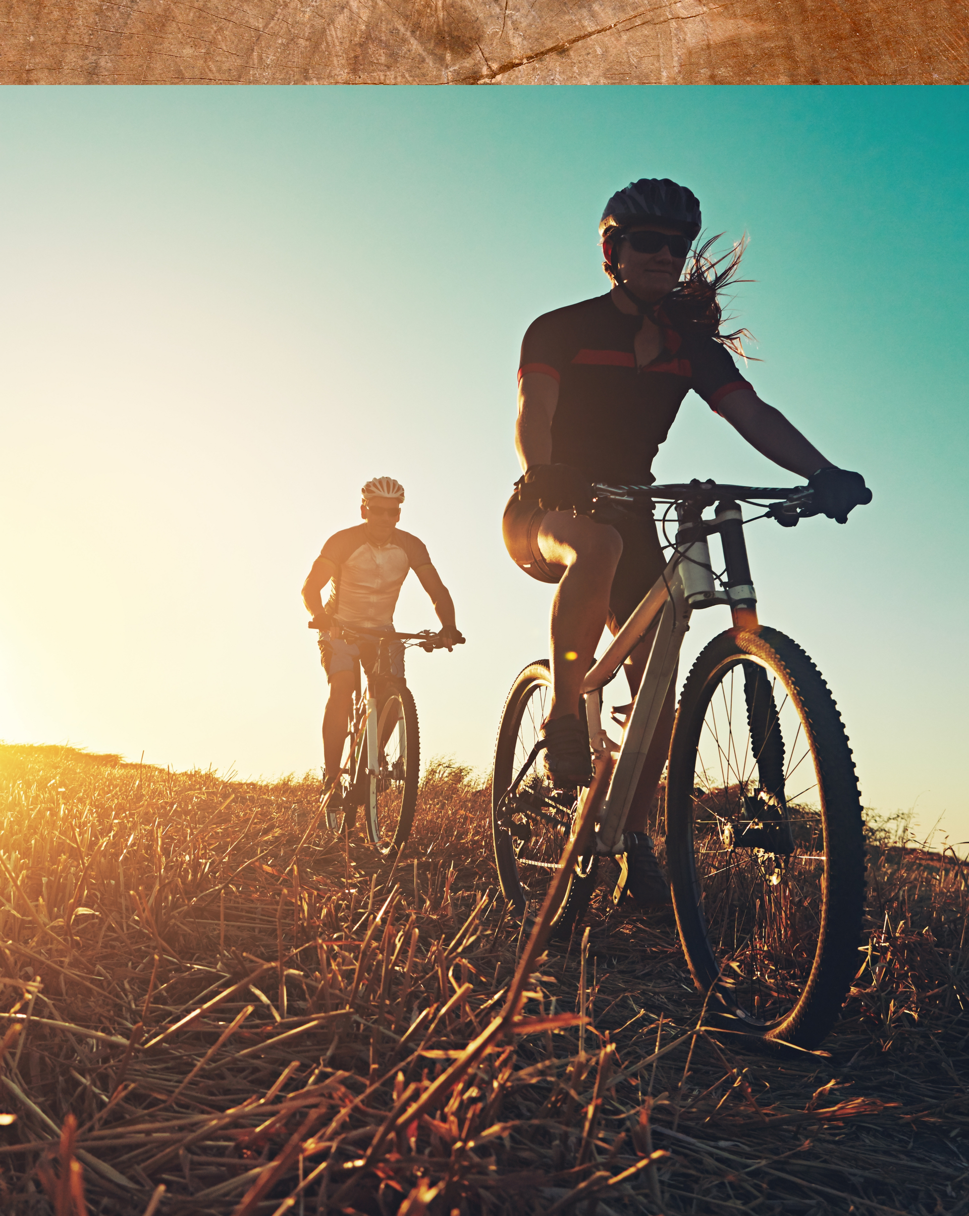 Two people are riding bicycles in a field at sunset.