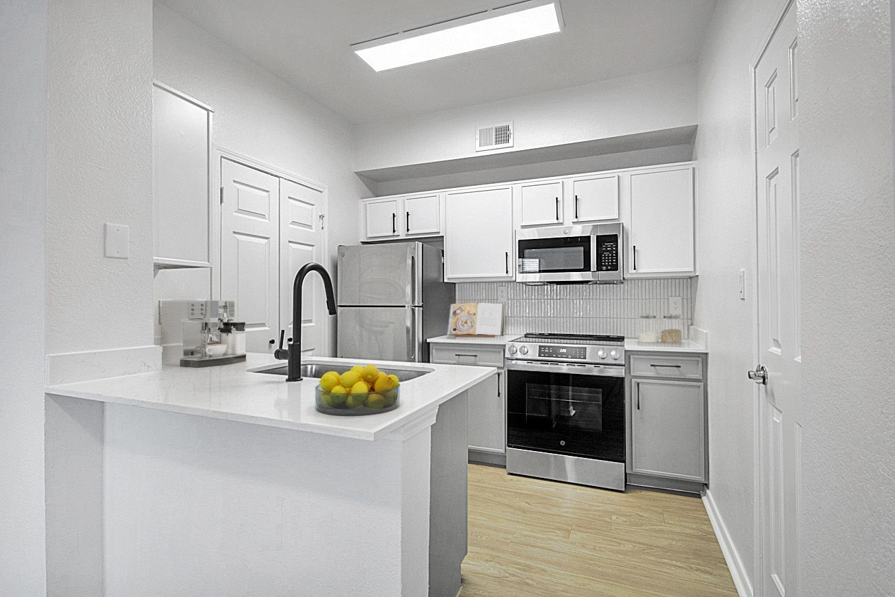Modern, white kitchen with stainless steel appliances and a countertop island, bathed in bright light.