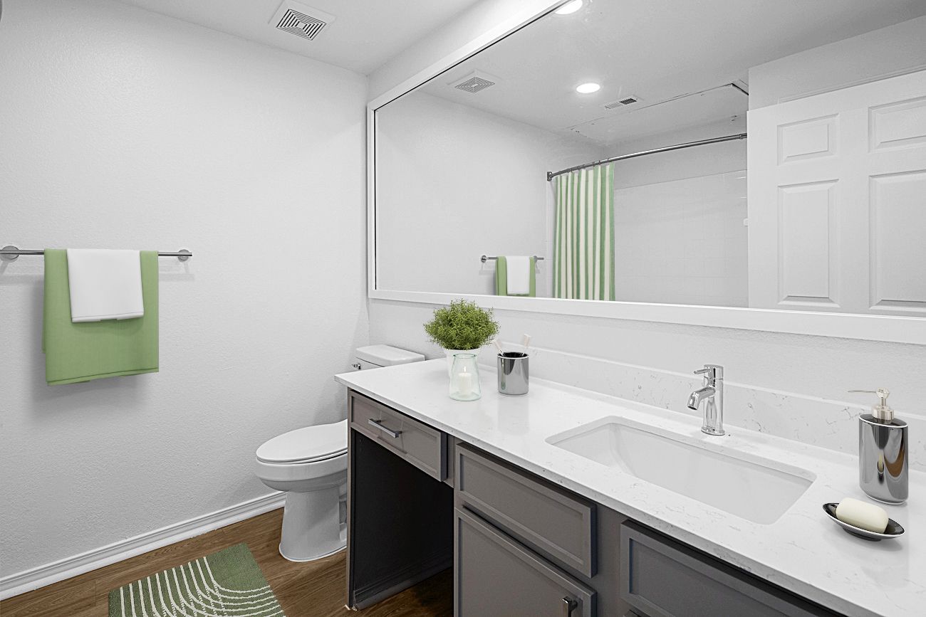 Bathroom with a white vanity, a large mirror, a toilet, and a towel rack with a green towel.