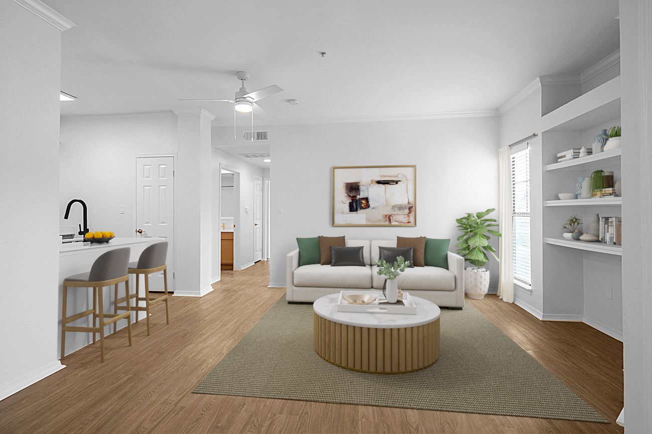 Bright, modern living room with a beige sofa, round coffee table, and built-in shelves. Open to a kitchen with a bar.
