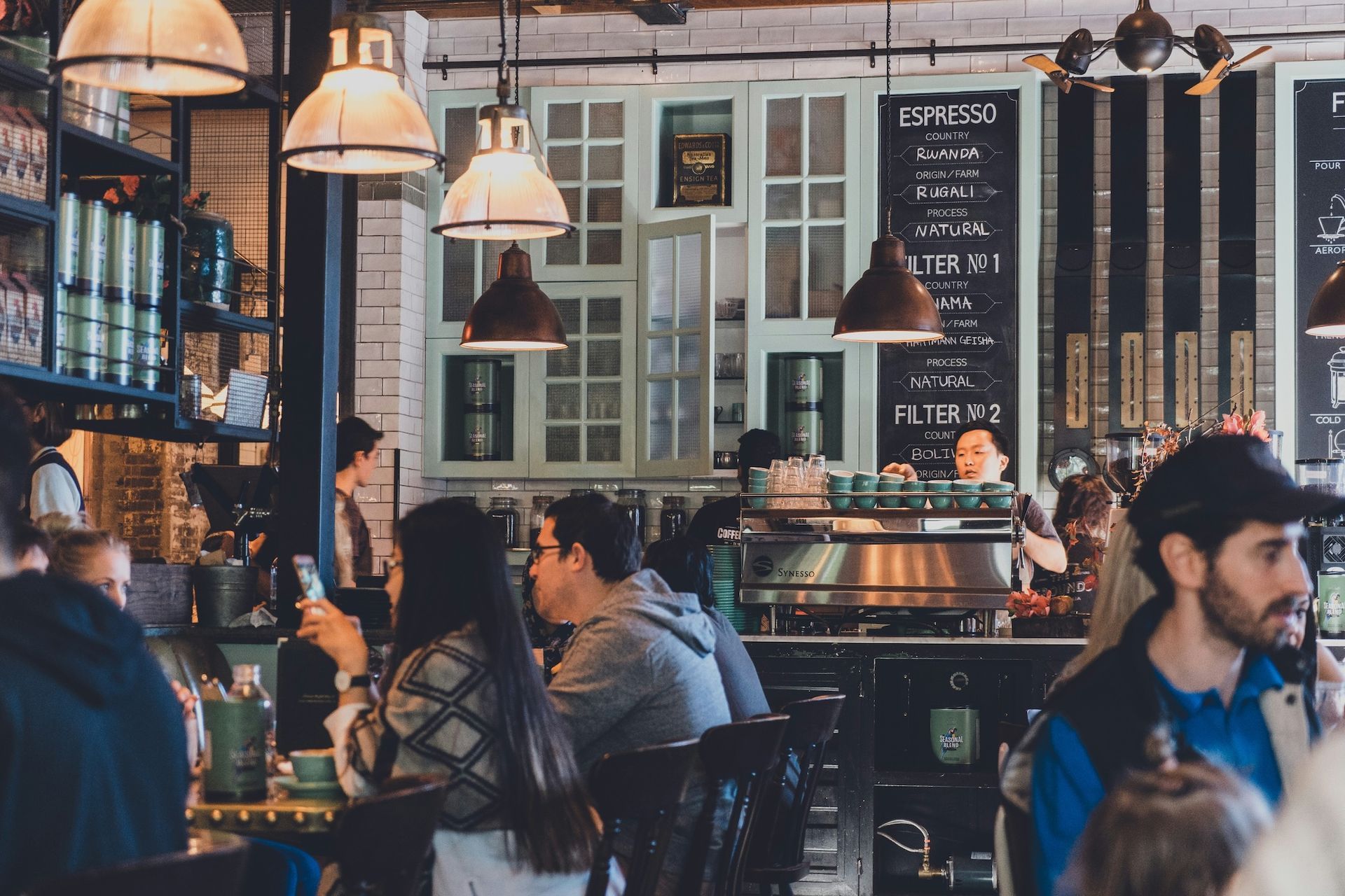 Busy coffee shop interior with customers, barista, and coffee machine.