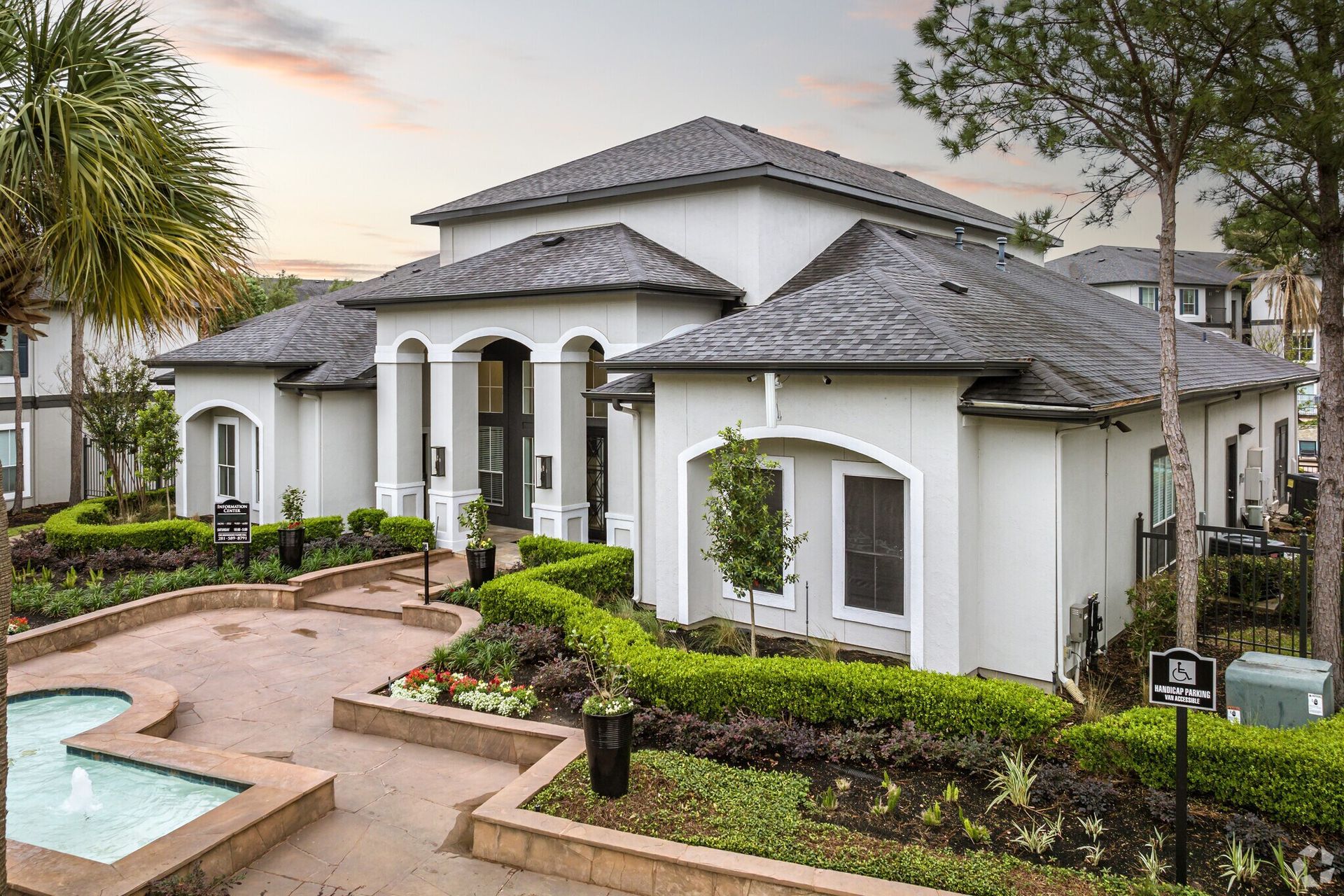 White building with dark roof, arched entry, fountain, and manicured landscaping.