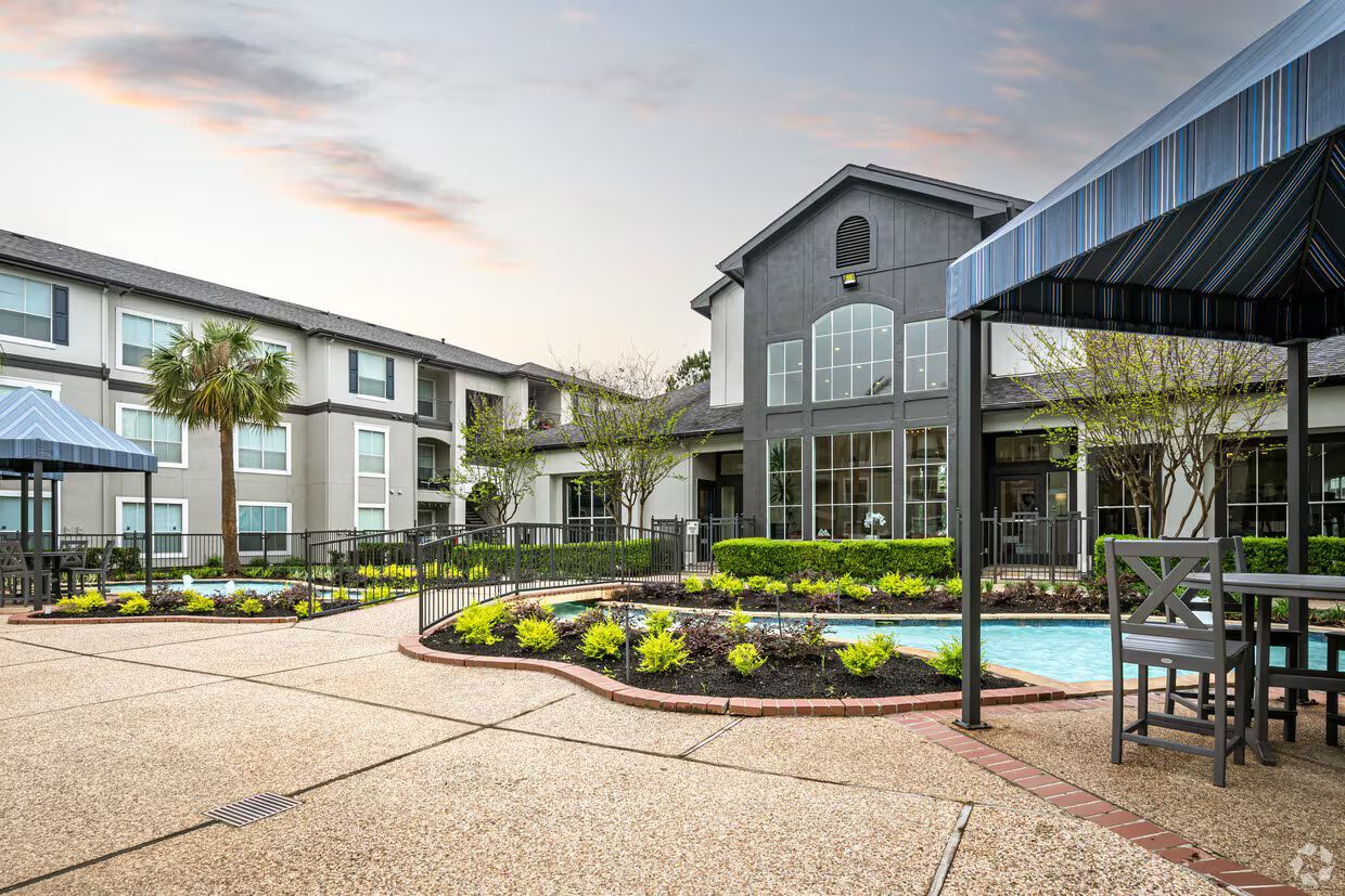 Courtyard with a pool, two-story buildings, and shaded seating under a cloudy sky.