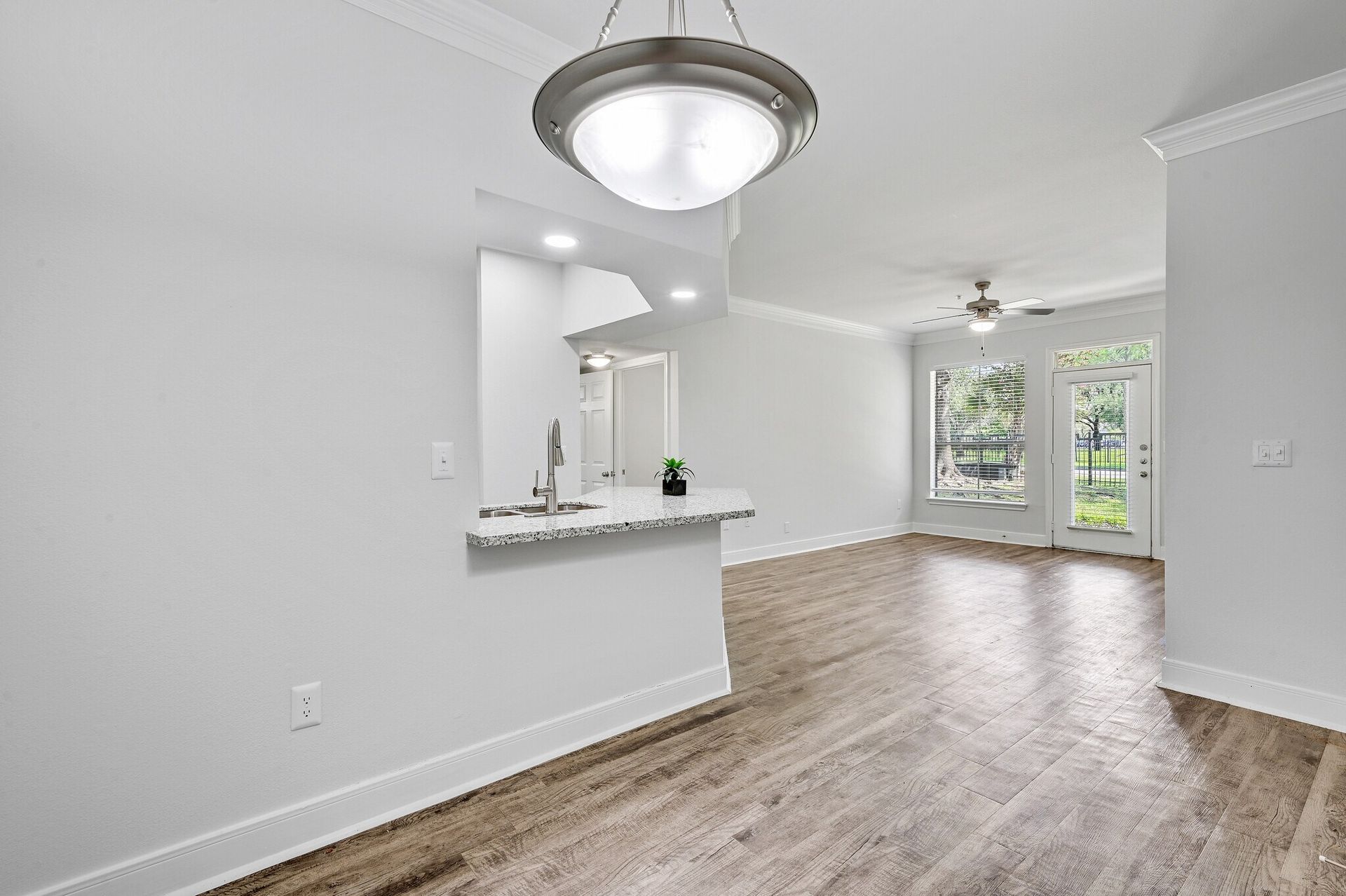 Bright, empty room with kitchen counter, light fixture, wood floors, and patio doors.