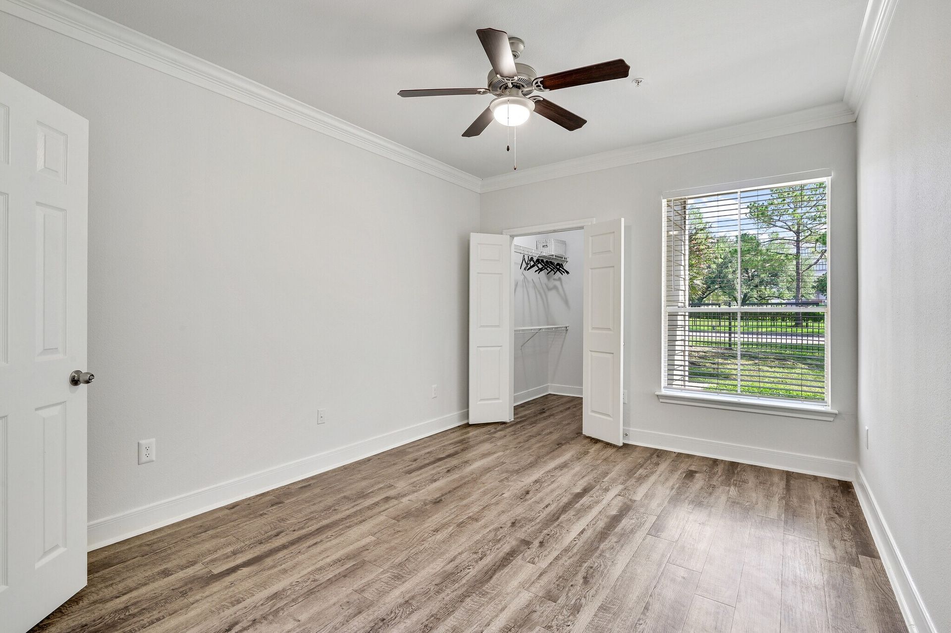 Empty bedroom with light wood-look flooring, white walls, and a ceiling fan. Includes a closet and window.