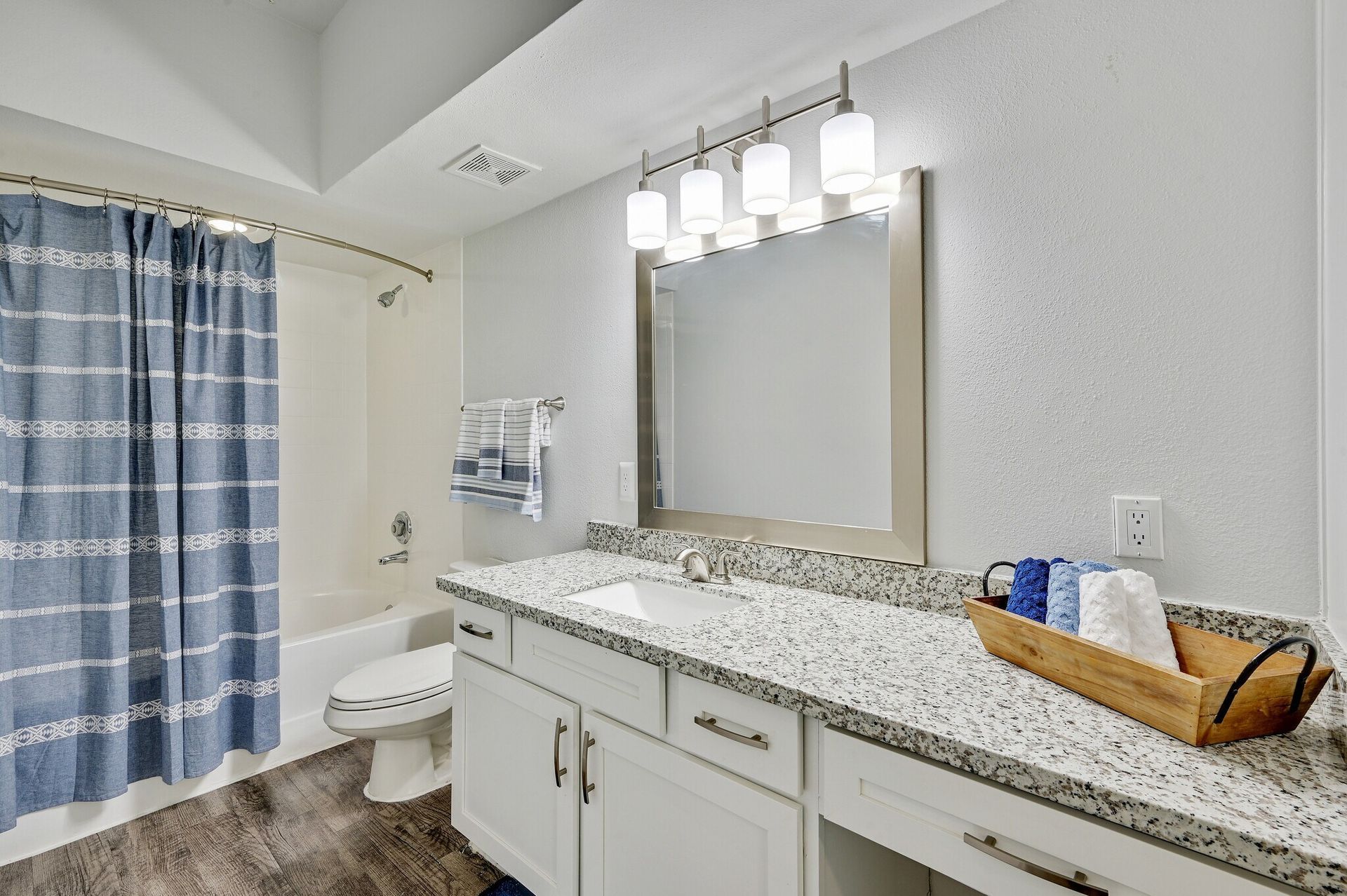 Bathroom with white vanity, speckled countertop, large mirror, shower with striped curtain.