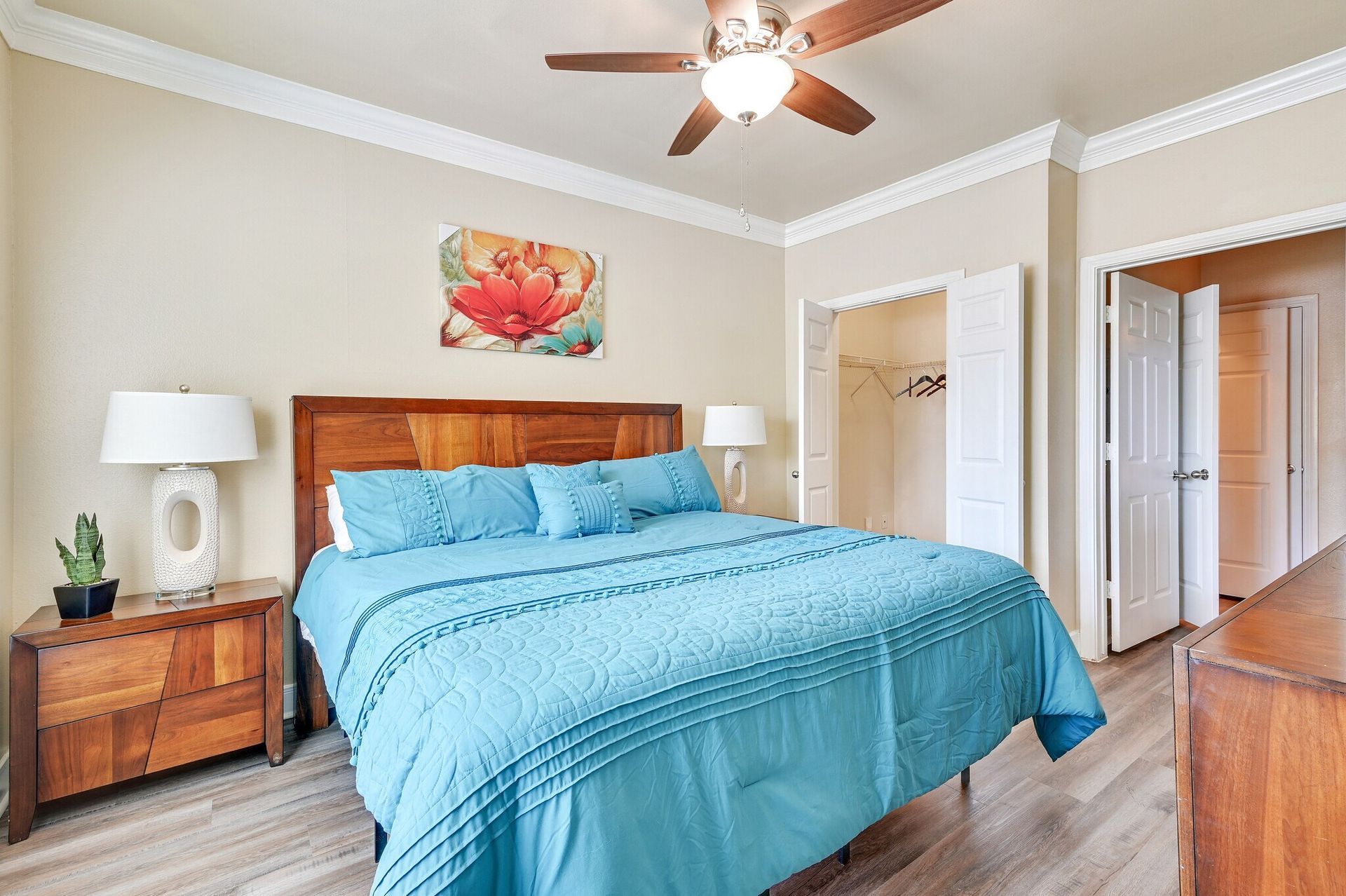 Bedroom with a blue bed, wooden furniture, artwork, and a ceiling fan.