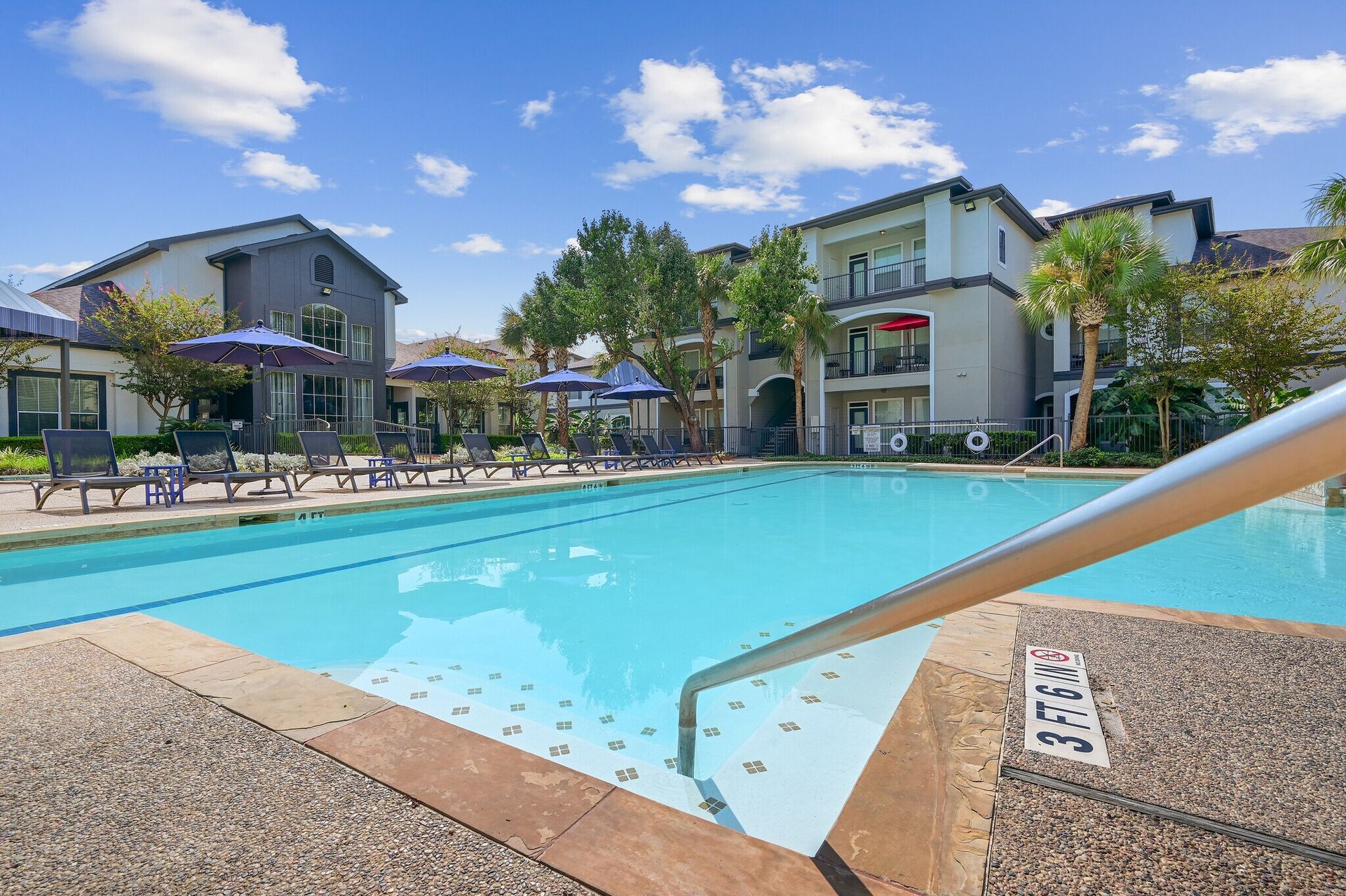 Swimming pool in front of apartment buildings with blue skies and lounge chairs.