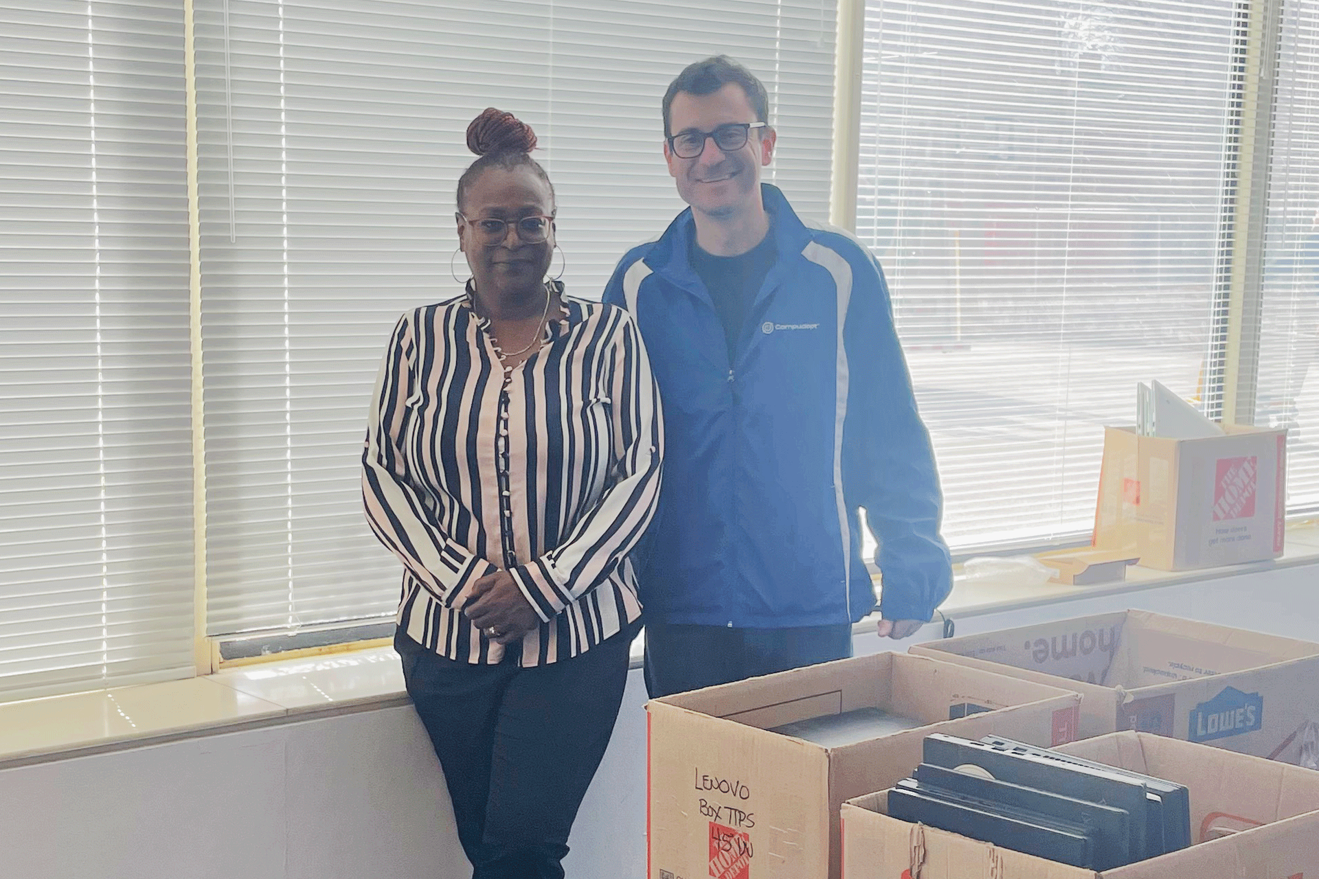 A woman and man stand behind a table with boxes full of laptops to give away