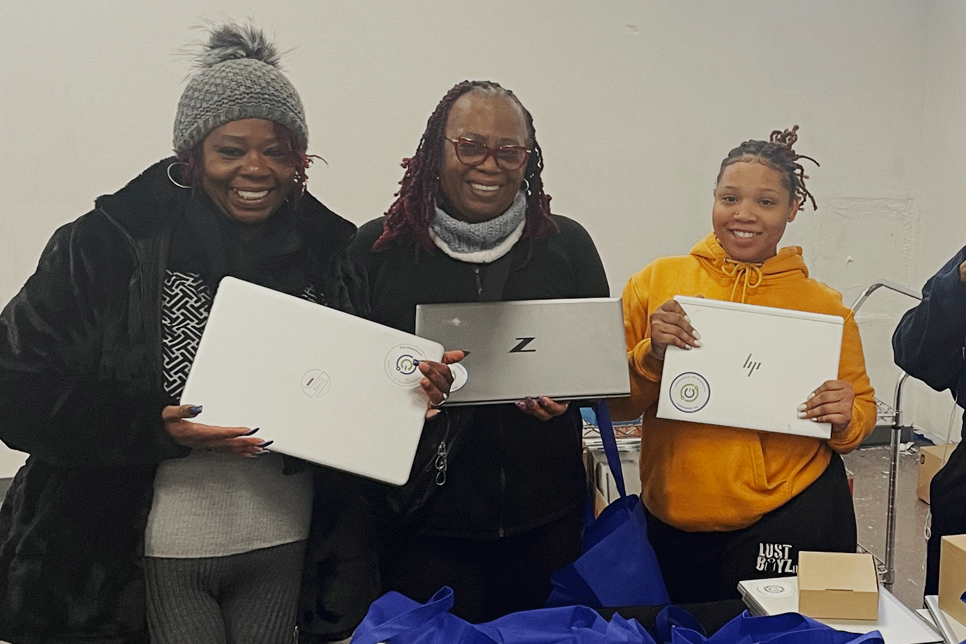 Three smiling women, each holding a laptop