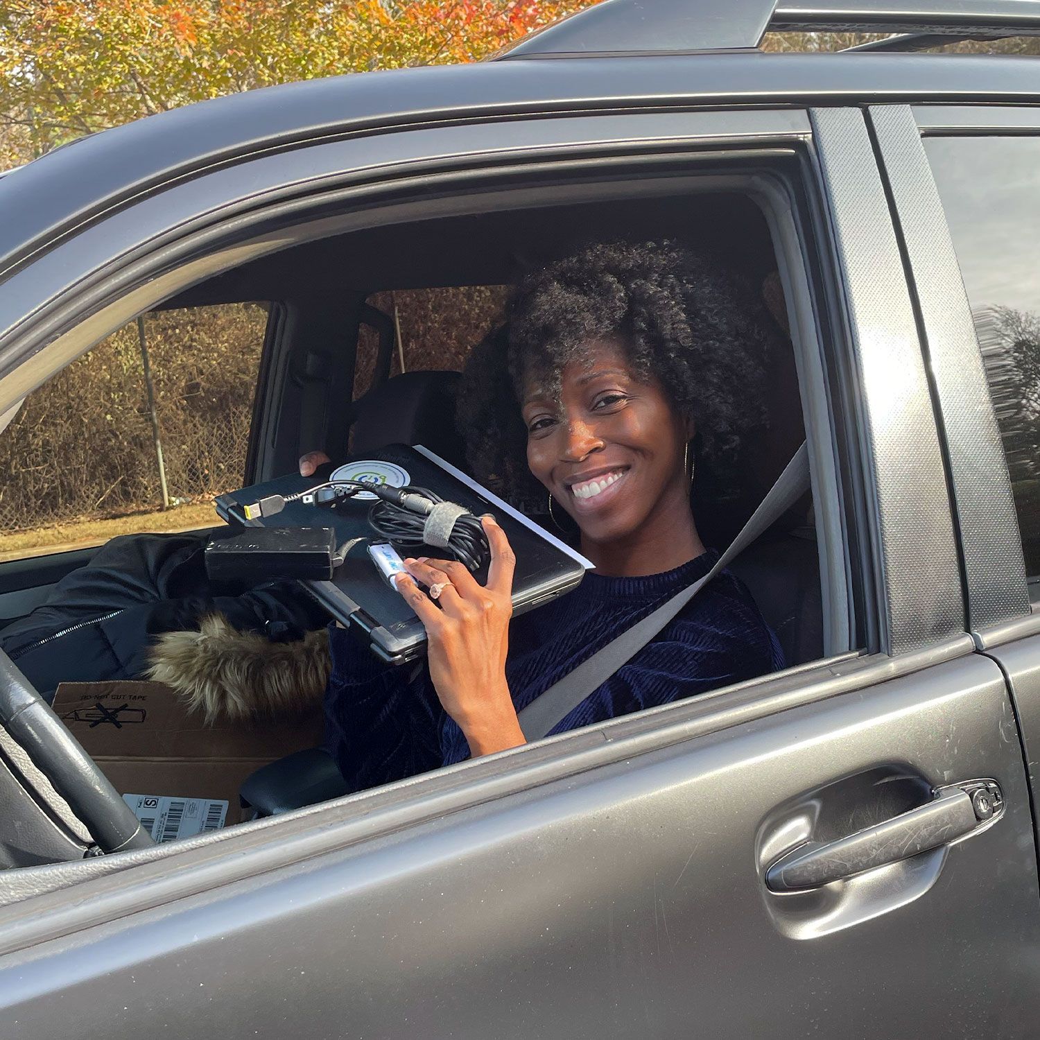 Happy woman in a gray car smiles, holding a free laptop computer.