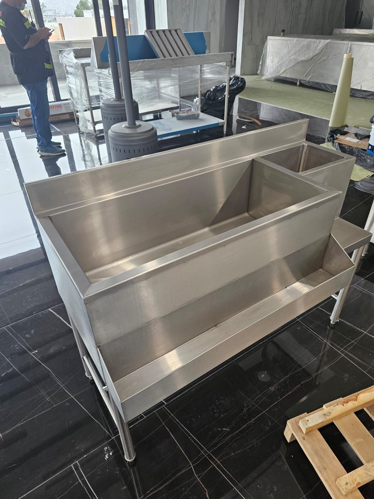 Un hombre está de pie junto a un gran fregadero de acero inoxidable en una habitación.