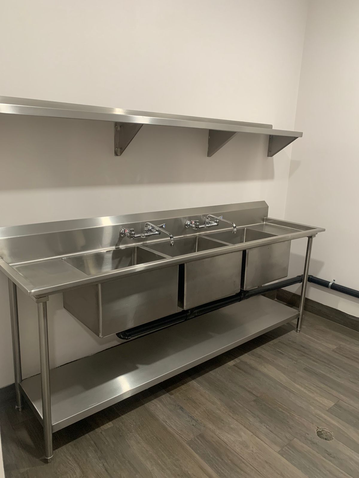 Fregadero de cocina de acero inoxidable con tres fregaderos y una balda.