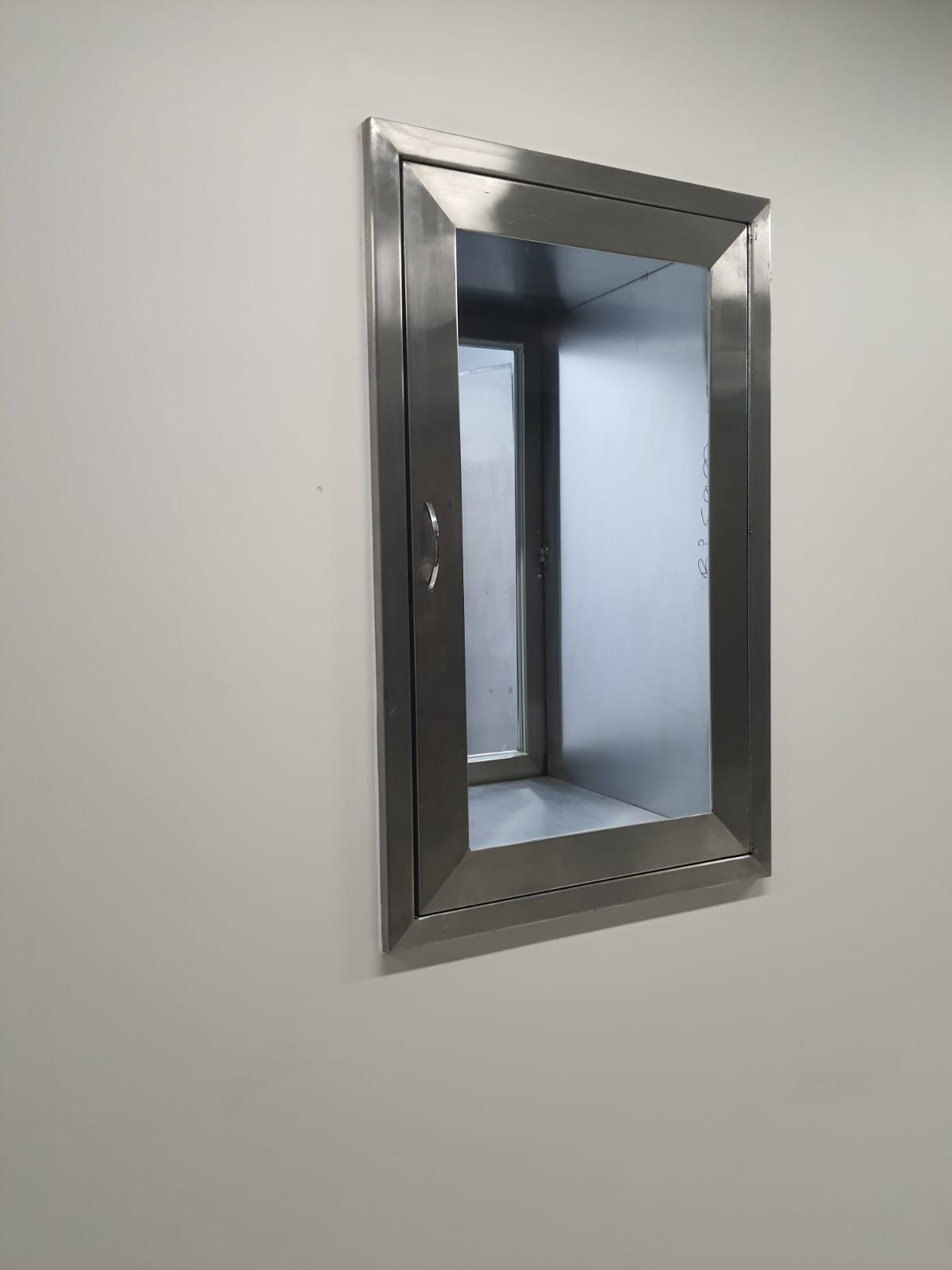 Un espejo de acero inoxidable cuelga de una pared blanca.