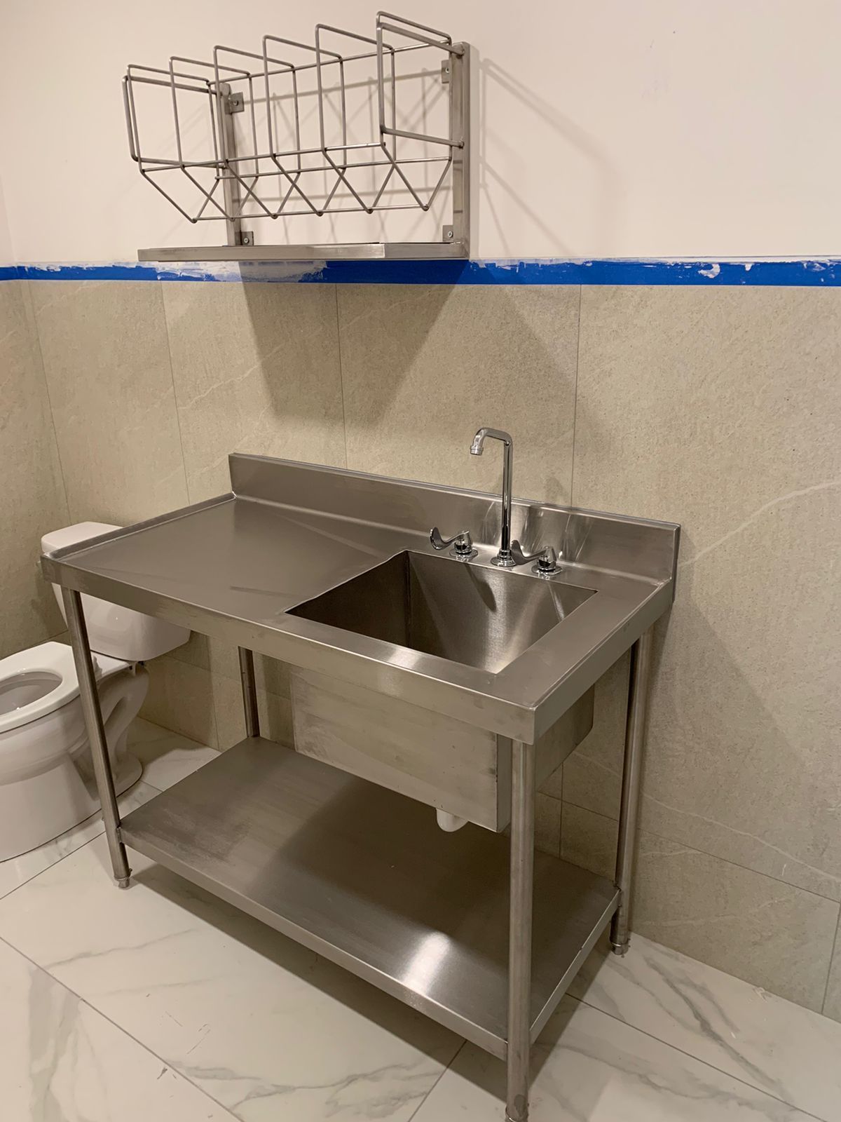 Un lavabo y una encimera de acero inoxidable en un baño junto a un inodoro.