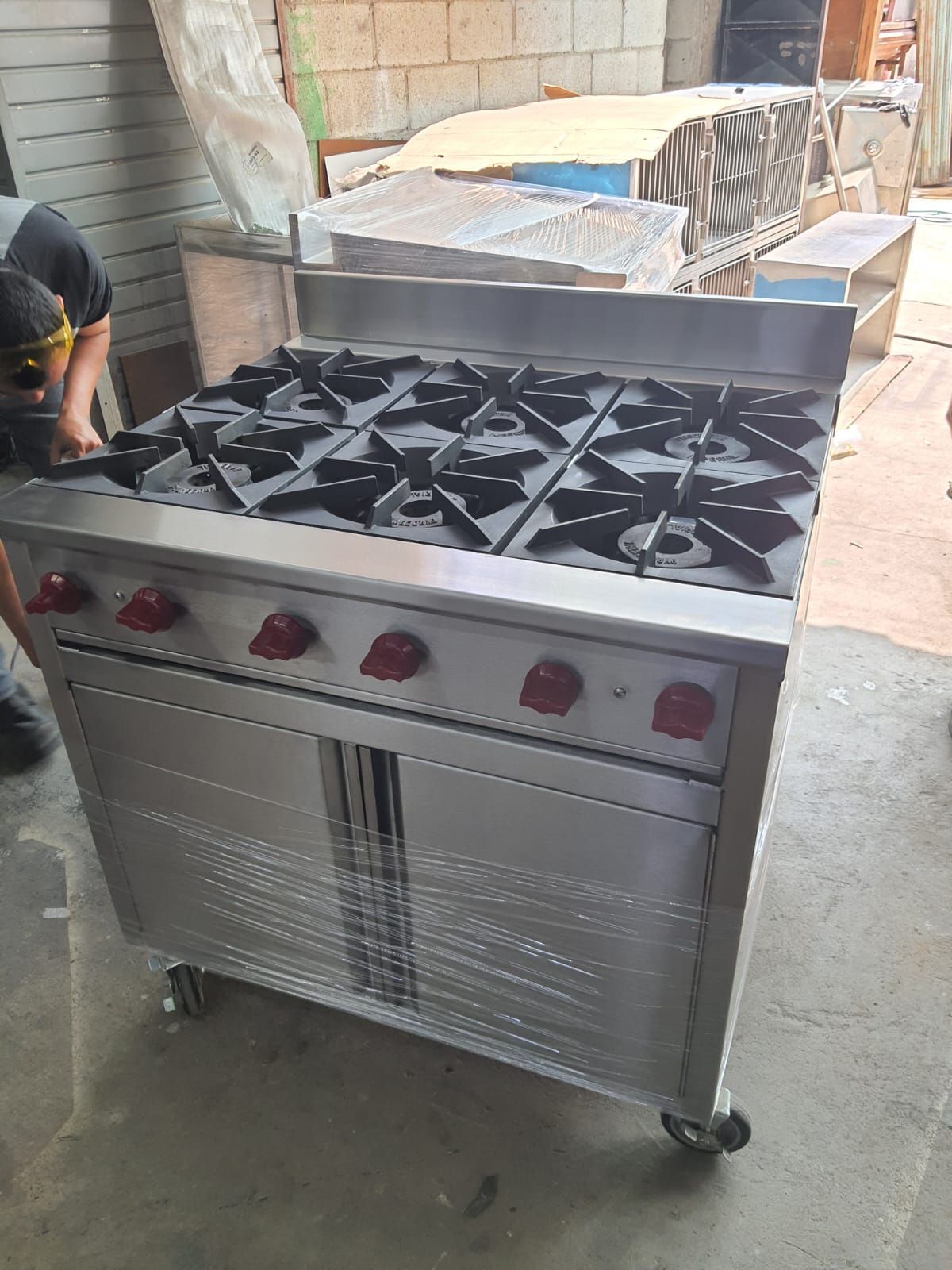 Sobre un suelo de cemento hay una estufa de acero inoxidable con cuatro quemadores y un horno.