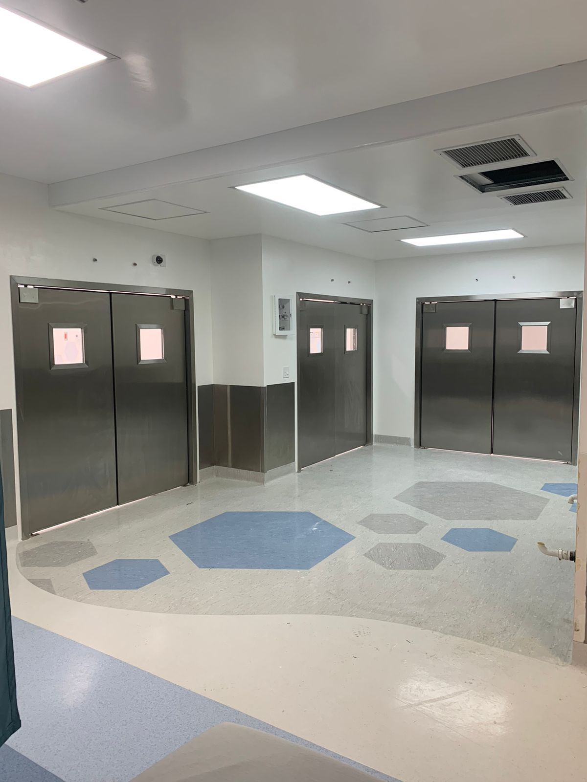 Un pasillo de hospital con puertas de acero inoxidable y suelo azul y blanco.