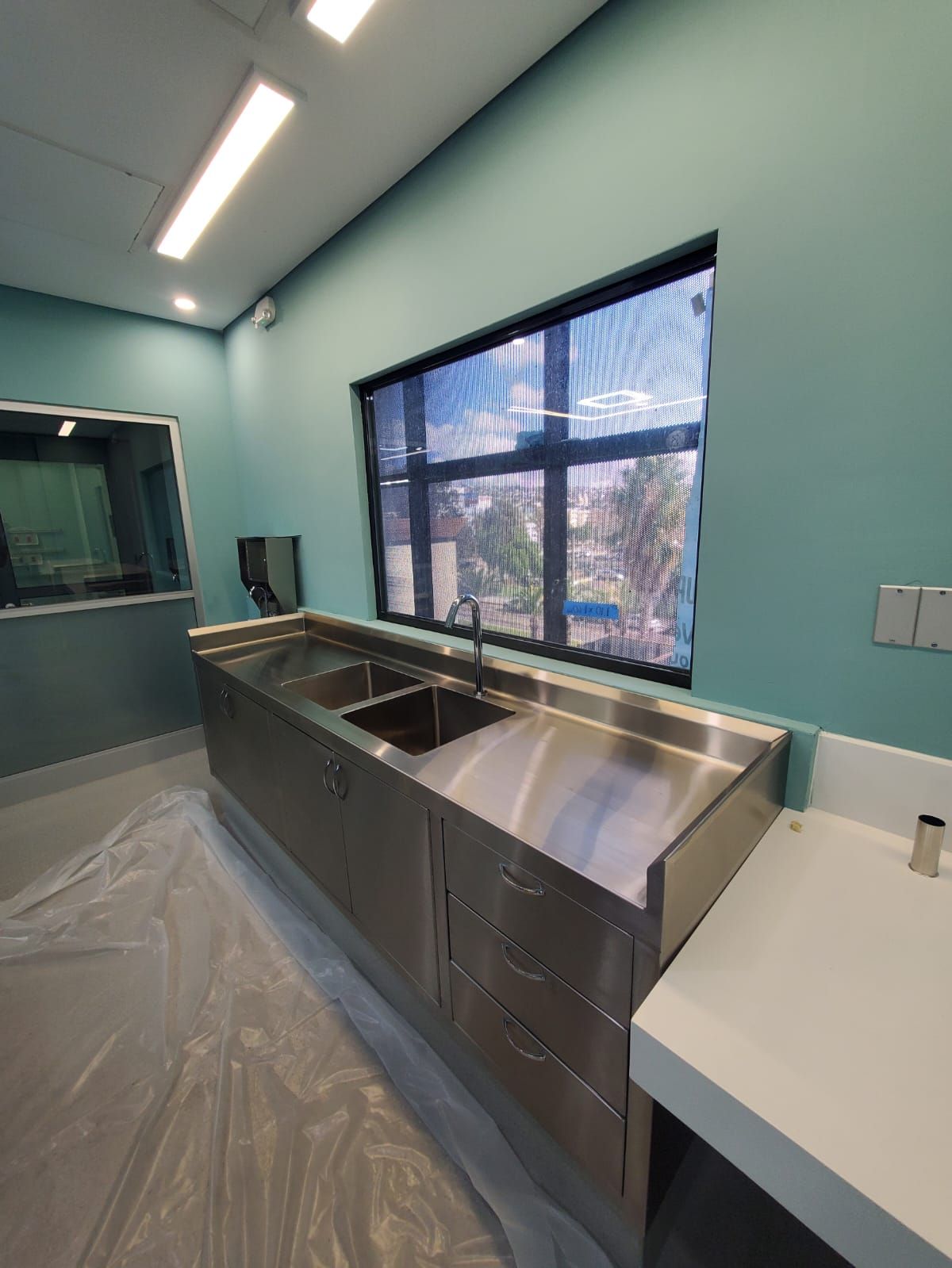 Una cocina con muebles de acero inoxidable, fregaderos, cajoneras y un gran ventanal.