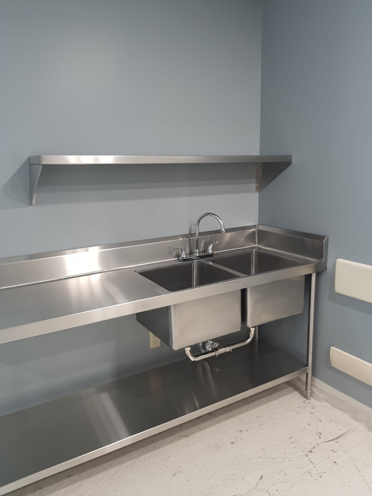 Una encimera de cocina de acero inoxidable con dos fregaderos y un estante.