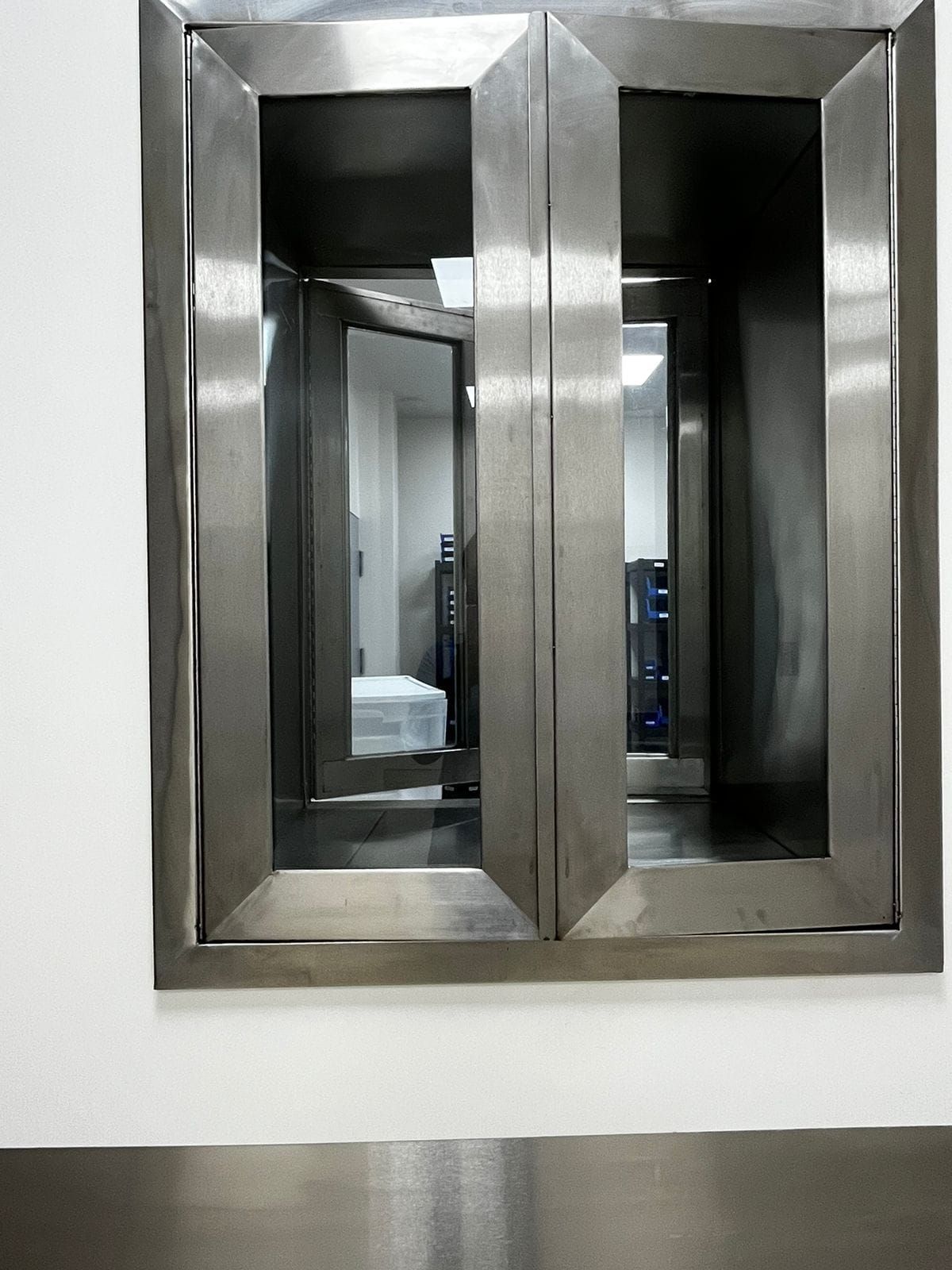 Una ventana de acero inoxidable con el reflejo de una cama en ella.