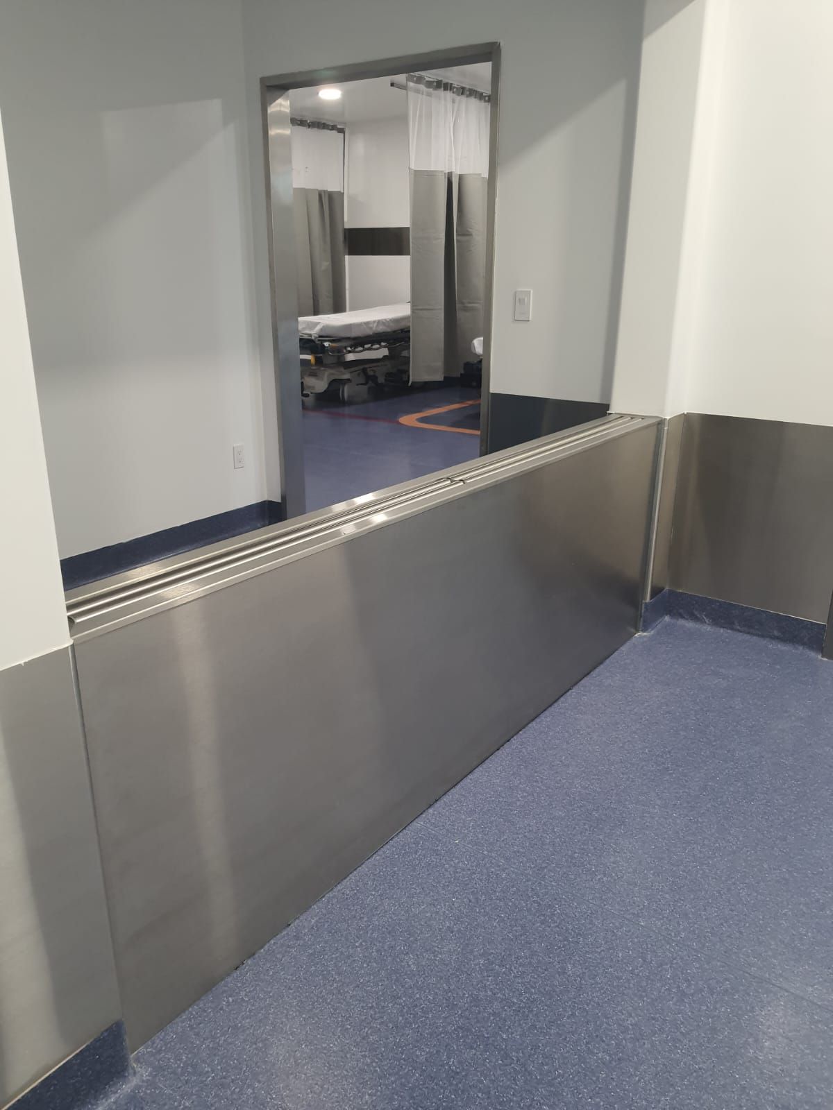 Una habitación de hospital con paredes de acero inoxidable y suelo azul.