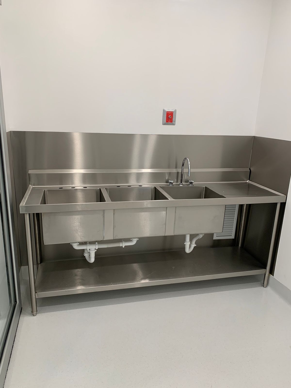 Un fregadero de acero inoxidable con tres lavabos y un grifo en una cocina.