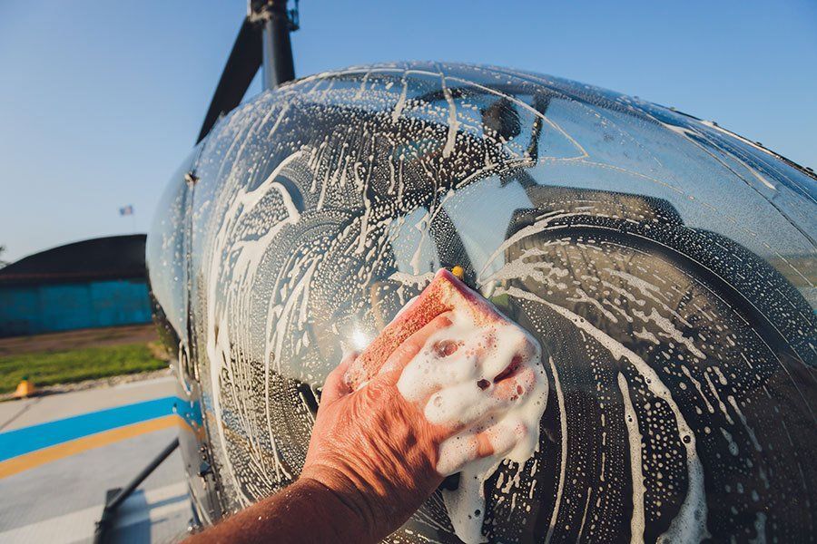 A person is washing a helicopter with a sponge.