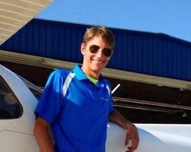 A man in a blue shirt and sunglasses is standing next to an airplane.