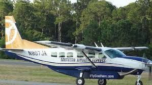 A small plane is parked on a runway in front of trees.