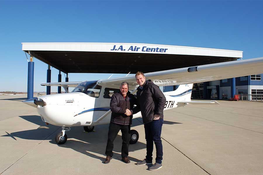 Two men are shaking hands in front of a small plane at the j.a. air center