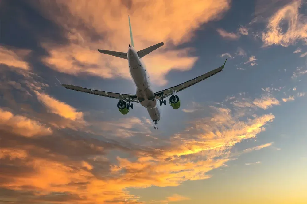 A large passenger jet is flying through a cloudy sky at sunset.