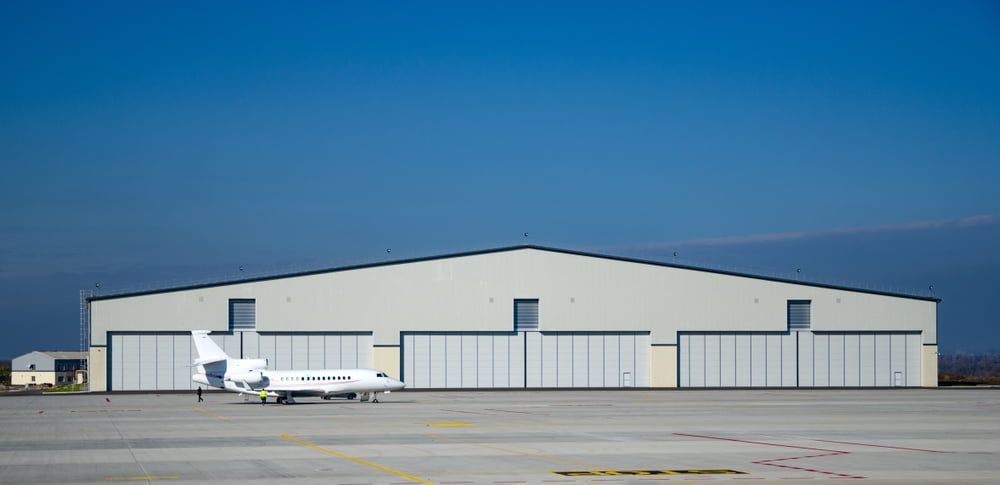 A small airplane is parked in front of a hangar at an airport.