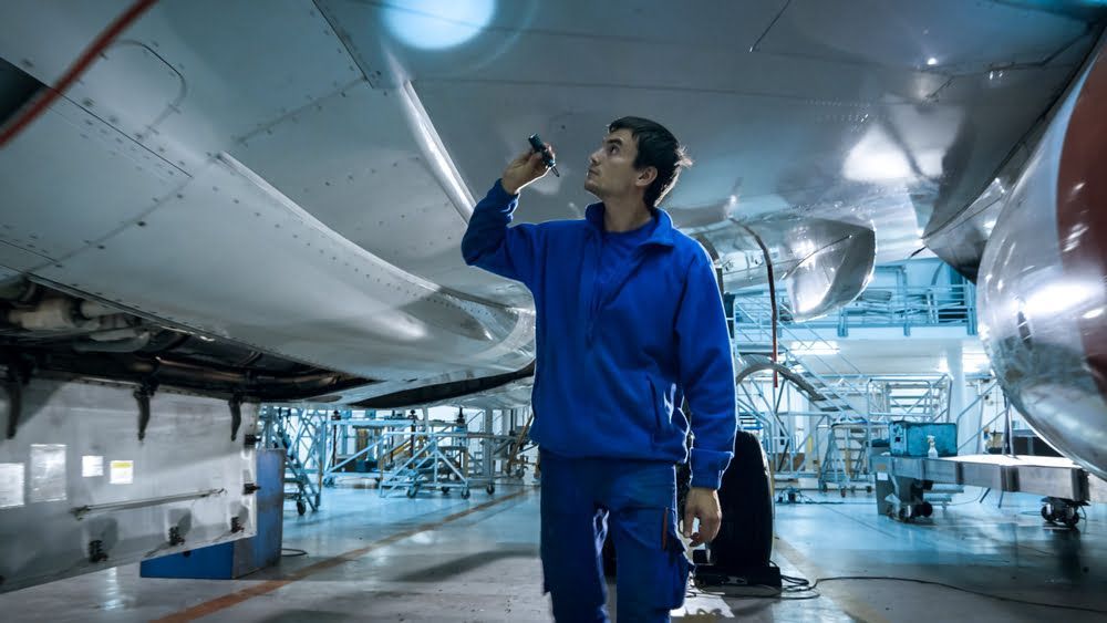 A man in a blue jacket is working on an airplane in a hangar.