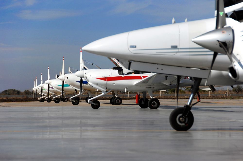 A row of small planes are parked on a runway