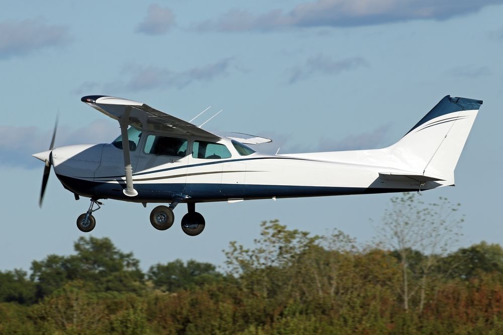 A small plane is flying over a field with trees in the background