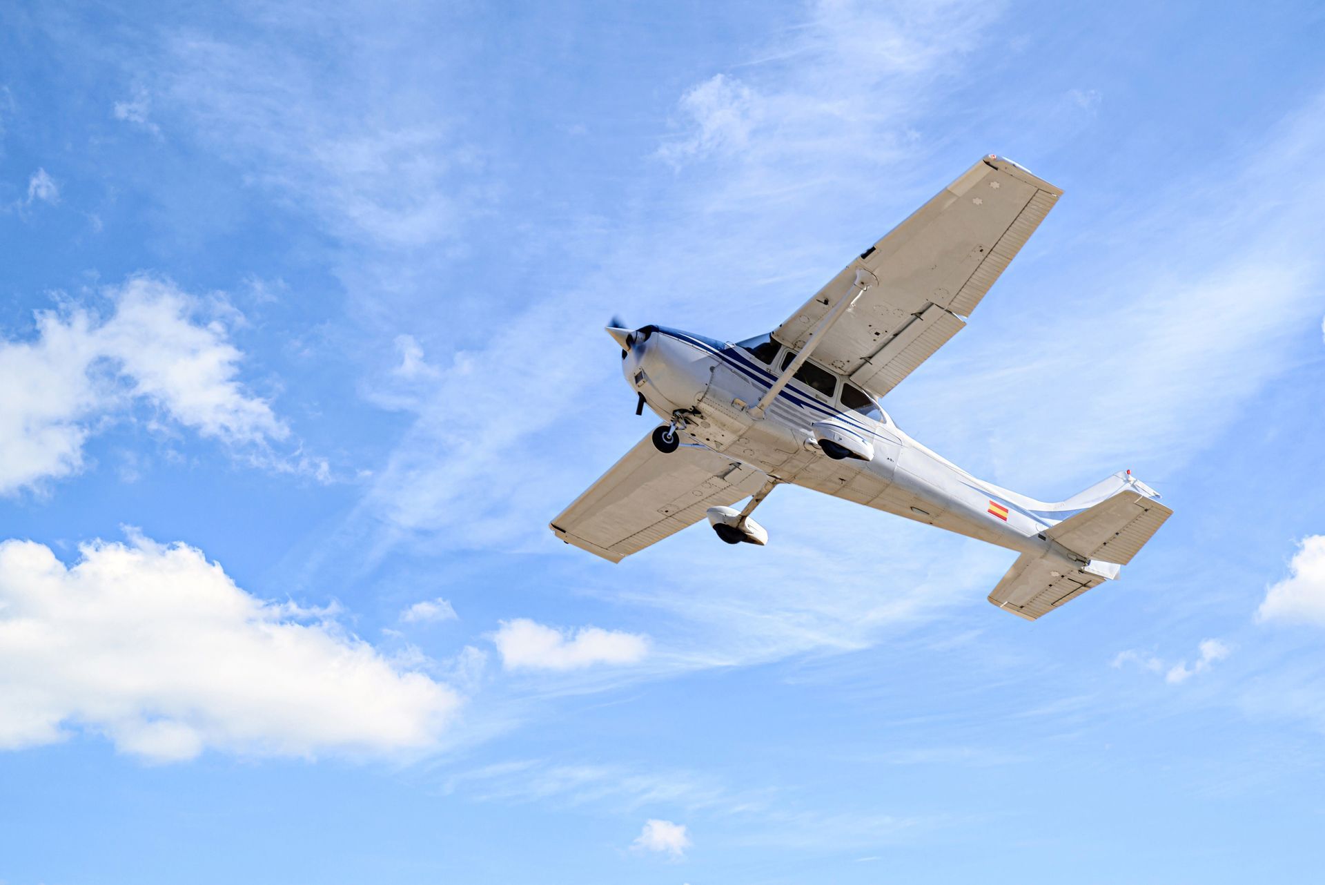 A small plane is flying through a blue cloudy sky.