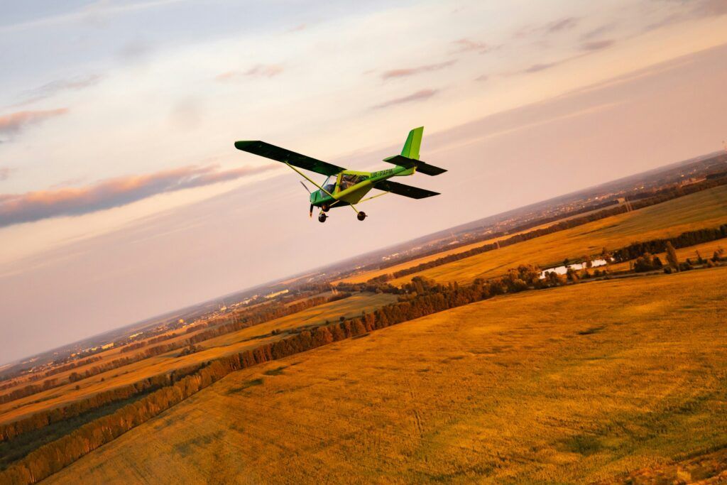 A small plane is flying over a field at sunset.