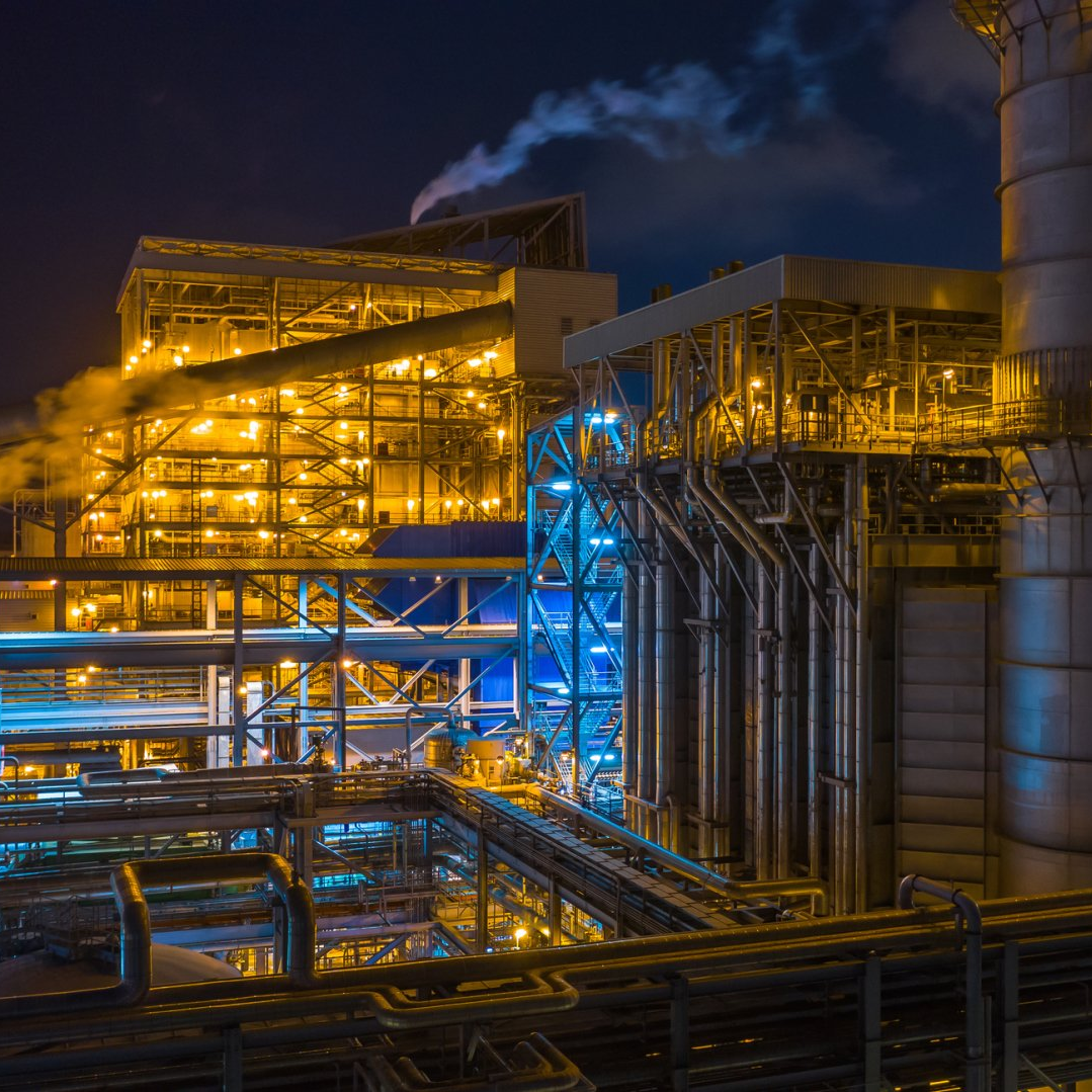 A large factory with lots of pipes and smoke coming out of it at night.