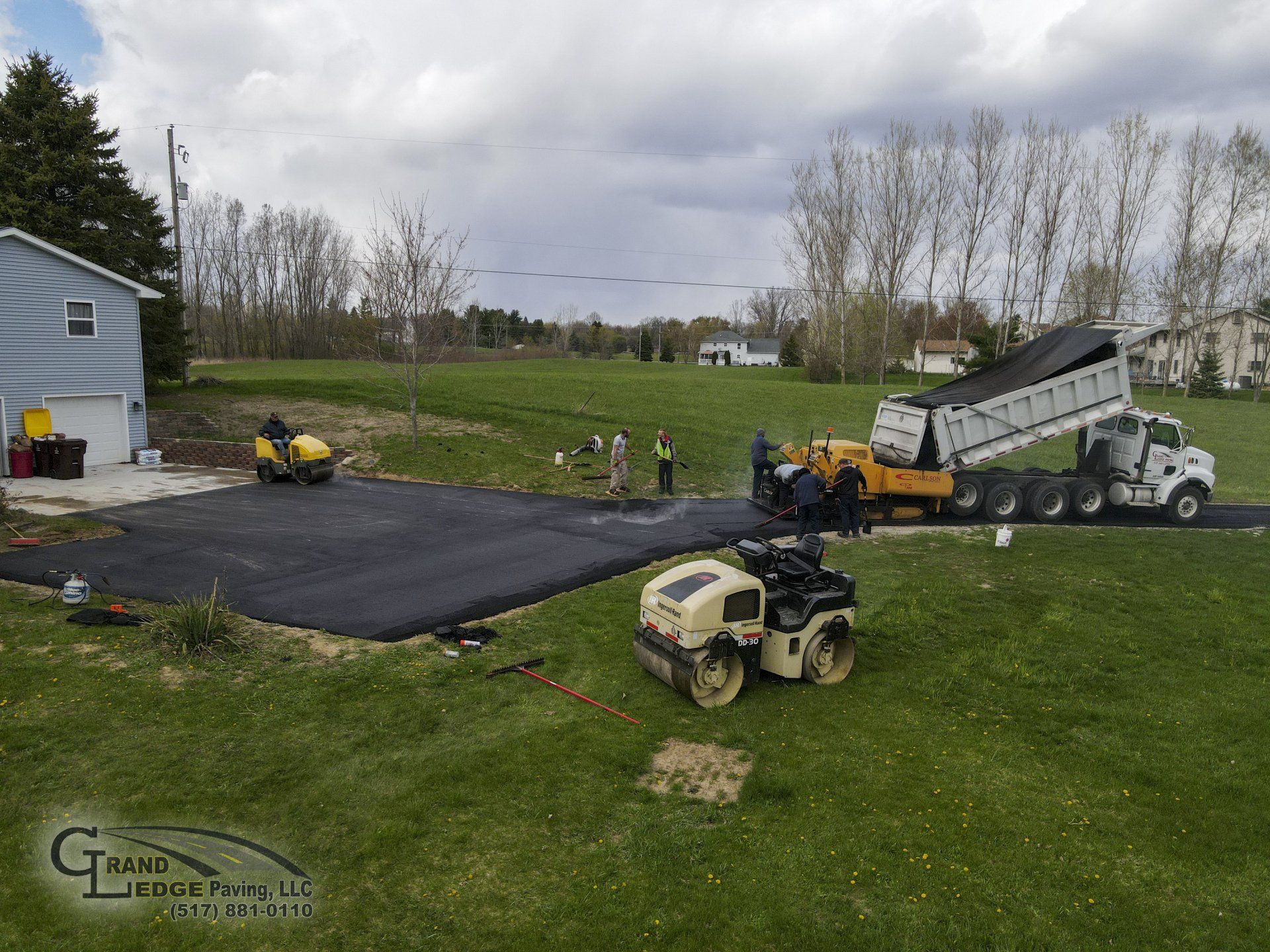 A dump truck is being loaded with asphalt in a driveway.